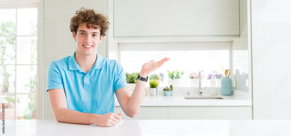 Wide shot of young handsome man at home smiling cheerful presenting and pointing with palm of hand looking at the camera. Wide shot of young handsome man at home smiling cheerful presenting and pointing with palm of hand looking at the camera.