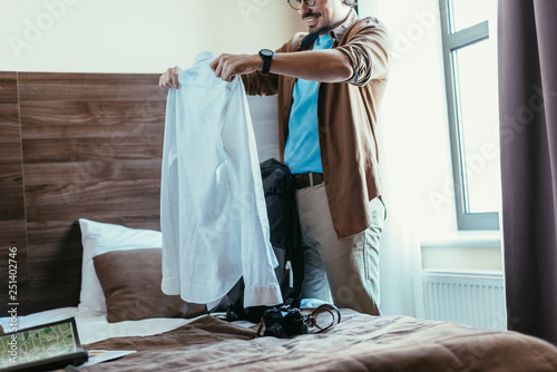 male tourist putting shirt into backpack in hotel room