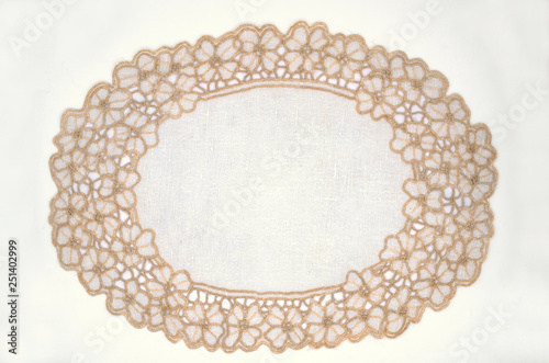 Oval openwork white napkin with cream flowers on the edge of the cotton thread, lies on a white background