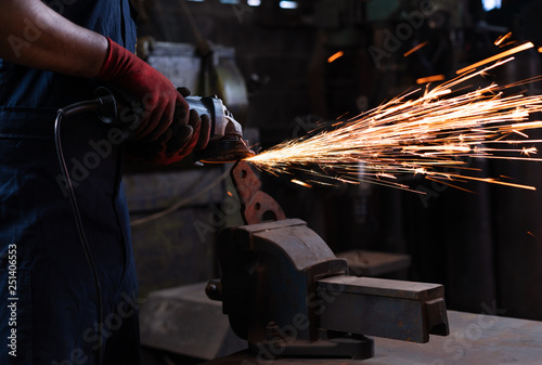 mechanical engineer technician operating an angle grinder power tool on metal clamped to a workshop vice with sparks flying