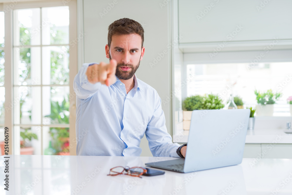 Handsome business man working using computer laptop pointing with finger to the camera and to you, hand sign, positive and confident gesture from the front