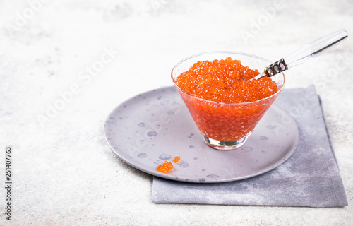  holidays composition. Red Salmon Caviar in glass bowl.  Festive Appetizer  on  gray background.Copy space for Text.