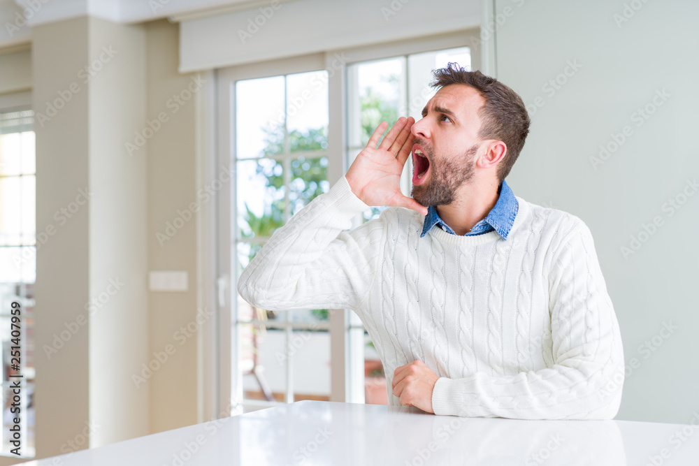 Handsome man wearing casual sweater shouting and screaming loud to side with hand on mouth. Communication concept. Handsome man wearing casual sweater shouting and screaming loud to side with hand on mouth. Communication concept.