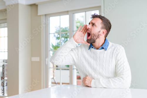 Handsome man wearing casual sweater shouting and screaming loud to side with hand on mouth. Communication concept.