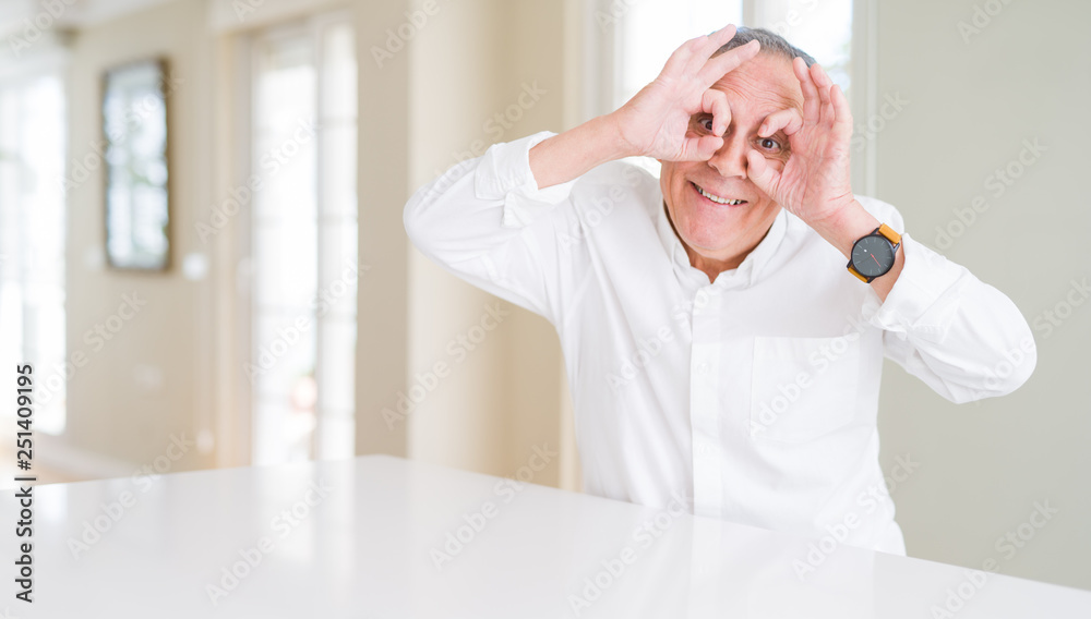 Handsome senior man at home doing ok gesture like binoculars sticking tongue out, eyes looking through fingers. Crazy expression. Handsome senior man at home doing ok gesture like binoculars sticking tongue out, eyes looking through fingers. Crazy expression.