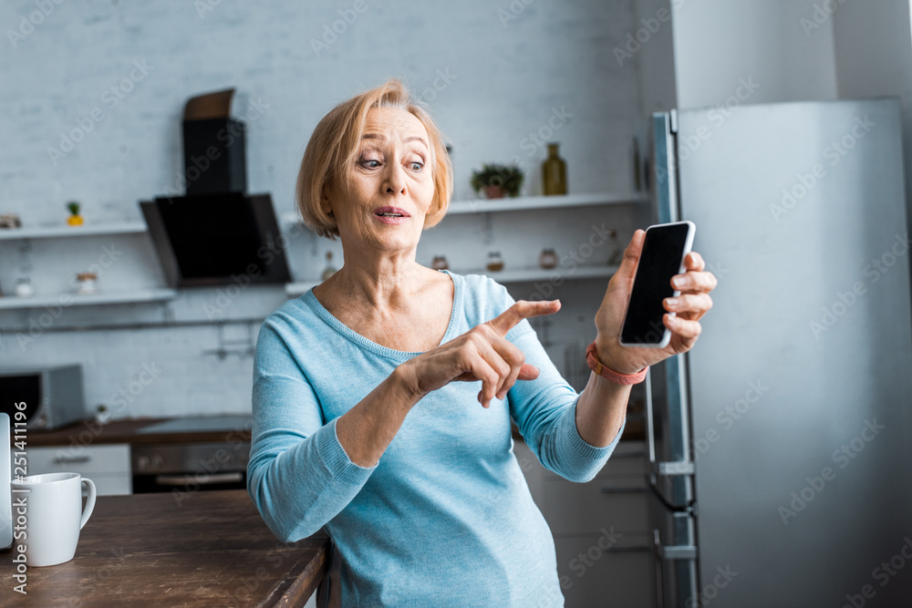 surprised senior woman pointing with finger at smartphone at home surprised senior woman pointing with finger at smartphone at home