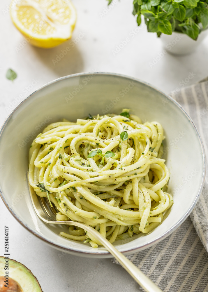 Pasta with avocado and Greek basil sauce in a ceramic bowl on a white table. Pasta with avocado and Greek basil sauce in a ceramic bowl on a white table.