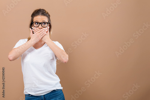 Young woman covering her mouth on a brown background