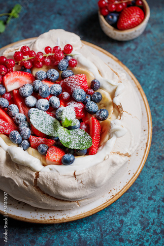 New Zealand Pavlova cake with whipped cream and mix of fresh berries on a blue textured background. photo