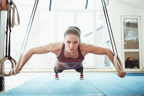Woman pushes-up on the rings in a clear gym infront of widow