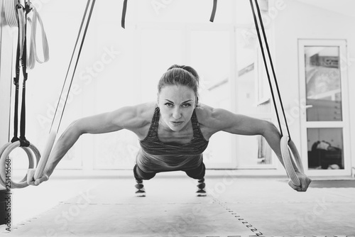 black and white photo of Woman pushes-up on the rings in a clear gym infront of widow