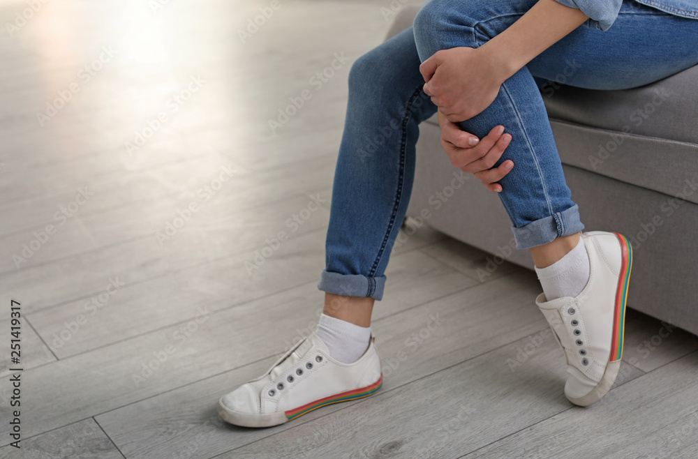 Young woman suffering from leg pain indoors, closeup with space for text Young woman suffering from leg pain indoors, closeup with space for text