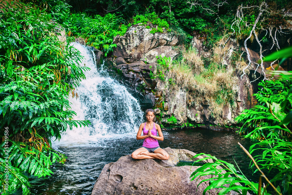 Yoga retreat woman praying doing the lotus pose meditating at waterfall