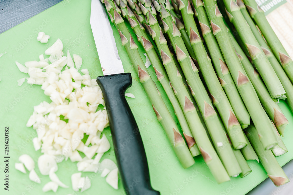 Fototapeta premium Fresh asparagus and garlic being prepared on a green cutting board