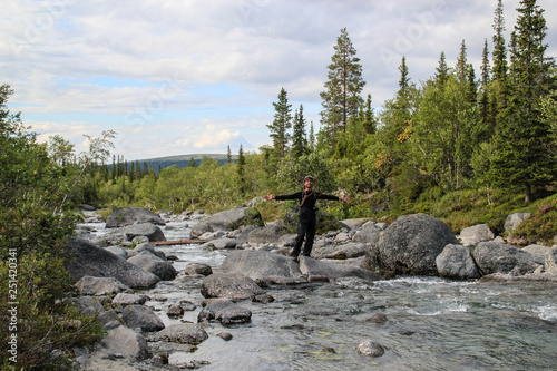 White Caucasian male tourist in sportswear stands in the middle of a mountain river with stones spread his arms