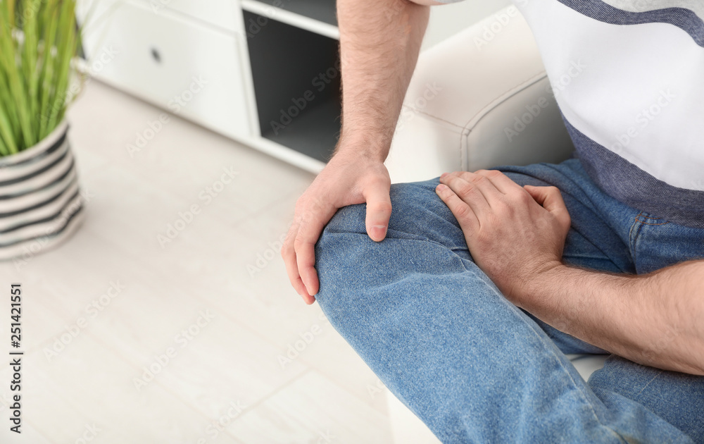 Young man suffering from leg pain indoors, closeup. Space for text