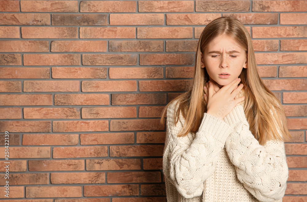 Teenage girl suffering from cough near brick wall. Space for text