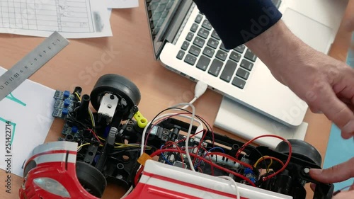 Teacher is helping and explaining schooler how fixing and assembling robotic model of a car. Classes in robotics for younger students