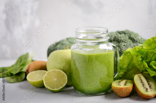 Fresh green smoothie in a jar with ingredients on a gray concrete background, selective focus.