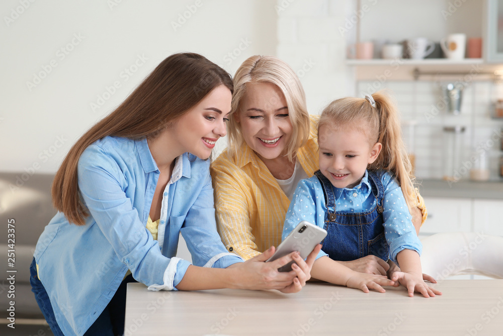 Portrait of young woman, her mother and daughter with smartphone at table indoors Portrait of young woman, her mother and daughter with smartphone at table indoors