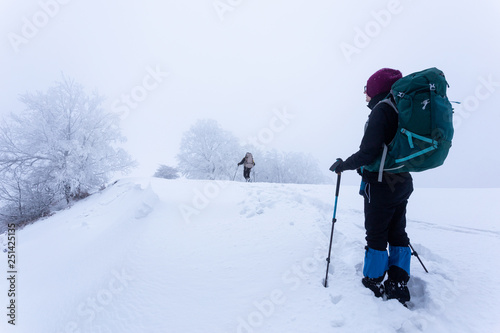 Young couple trekking together with their dog through the frozen mountains in Romania