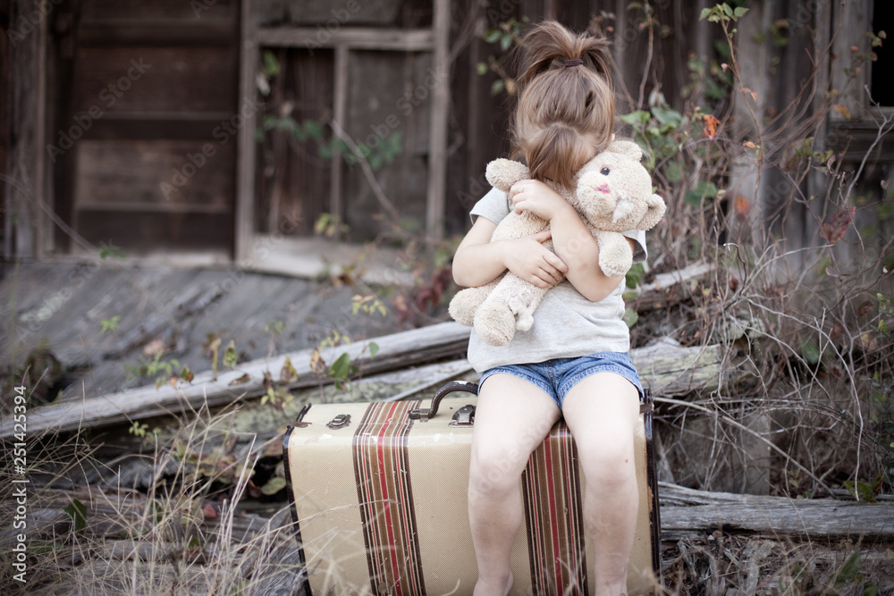 Fototapeta premium Little Girl with Ragged Teddybear and Suitcase - Poverty, Homelessness, Runaway Child