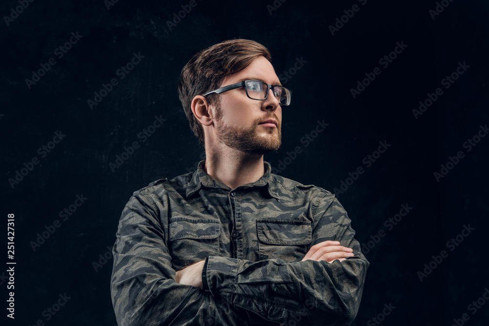 A confident hacker in a stylish military shirt posing with crossed hands and looking sideways. Studio photo with dark background A confident hacker in a stylish military shirt posing with crossed hands and looking sideways. Studio photo with dark background
