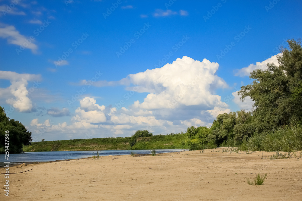 Beautiful summer landscape, sandy beach, river, blue sky and white big clouds.
