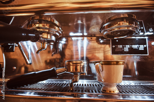Close-up photo of a portafilter and cup with cappuccino next to a coffee machine in the restaurant of a coffee shop photo