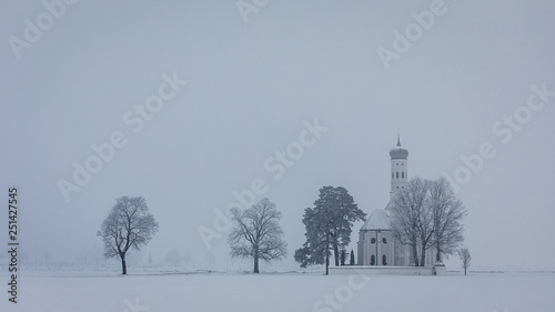 the beautiful snow covered little church st. coloman surroundet by fog photo
