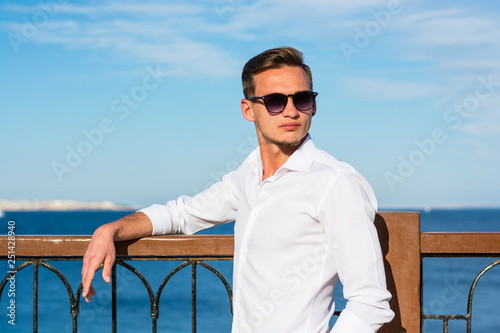 Young handsome man in man in a white shirt and white trousers at the sea background on a beach.