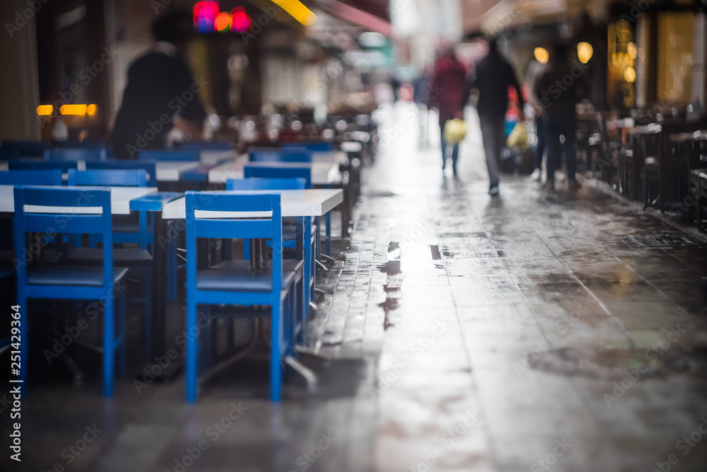 Pedestrians walk between cafes in the rain - obrazy, fototapety, plakaty 