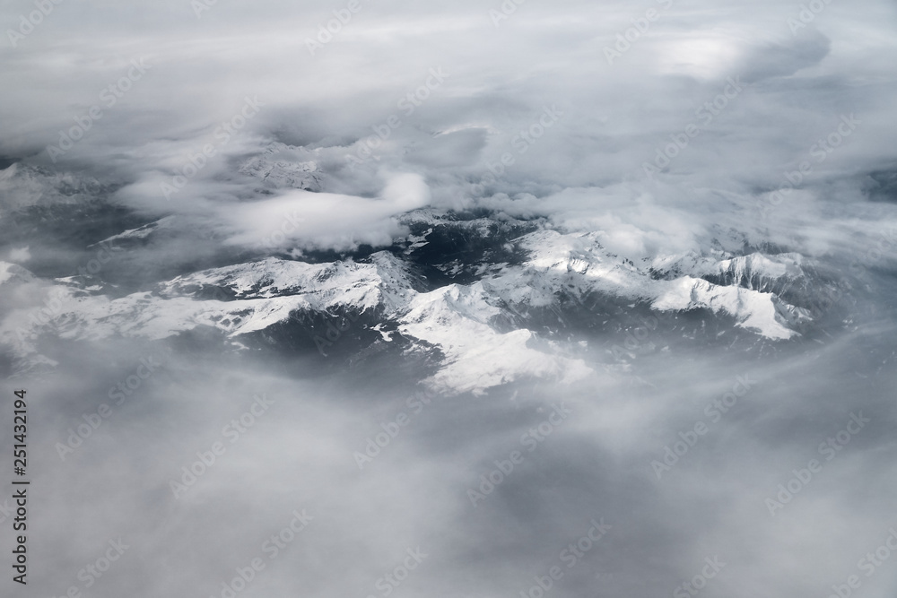 Aerial view of Alp's glaciers surrounded by moody clouds shot from the plane