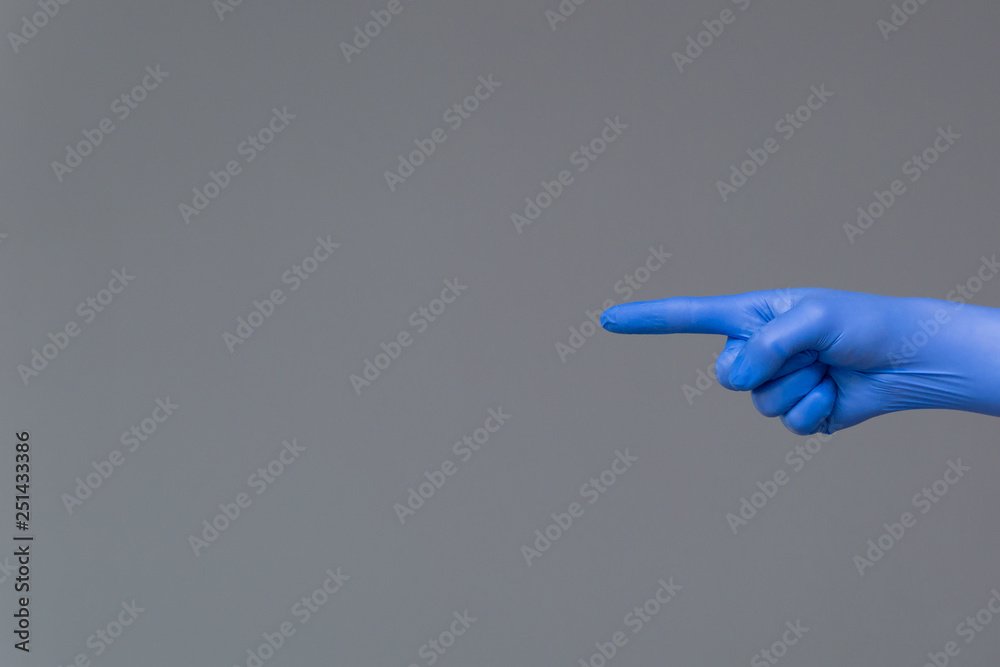 Hand in rubber glove points to the left with index finger. Neutral background , copy space. Hand in rubber glove points to the left with index finger. Neutral background , copy space.
