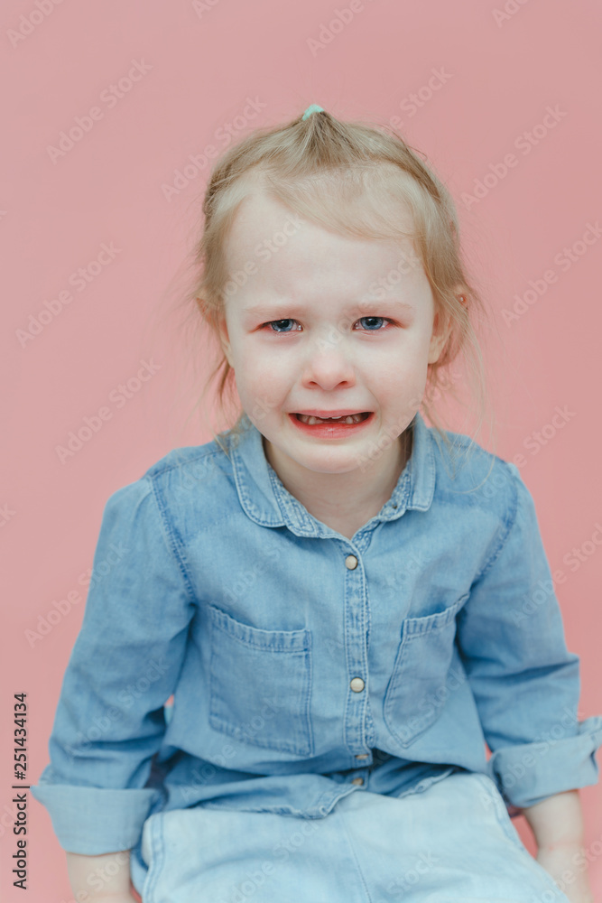Charming little girl in denim clothes crying on pink background Charming little girl in denim clothes crying on pink background