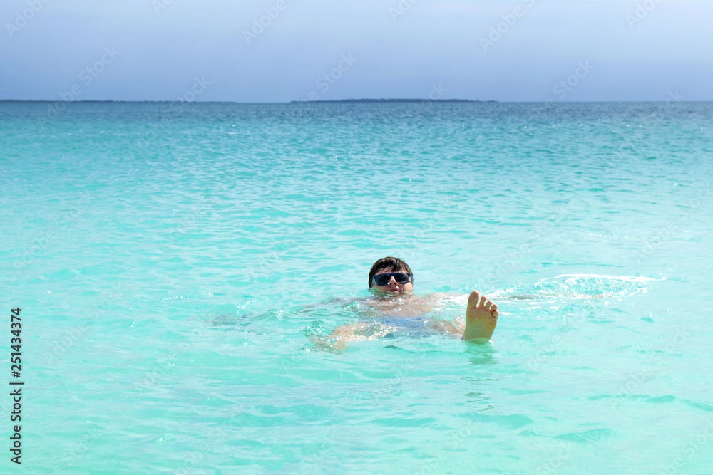 Funny attractive guy in sunglasses bathes in the ocean