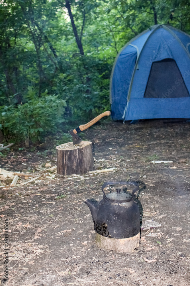 Camping, blue tent, ax in hemp and hiking kettle in the ashes Camping, blue tent, ax in hemp and hiking kettle in the ashes