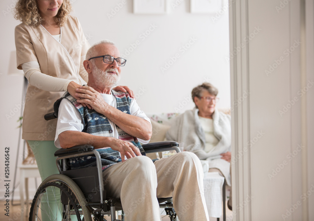 Senior man in a wheelchair assisted by a young nurse Senior man in a wheelchair assisted by a young nurse