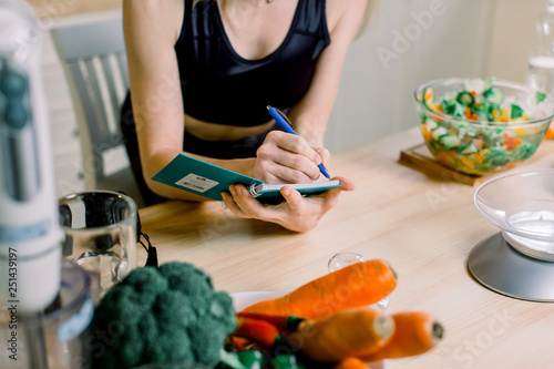 Young pretty woman in the kitchen at home writing shopping list . Modern kitchen, fresh vegetables and healthy food on the wooden table.