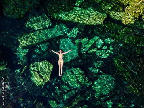 Overhead shot of a attractive young brunette woman in a bikini floating in the Cristalino cenote near Tulum, Mexico. photo
