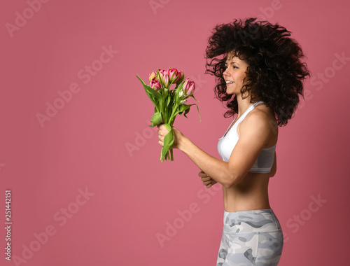 The sports girl runs on a pink background and carries a bouquet of tulips in her hand. The concept of spring renewal of the body and sport