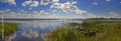 Summer panorama with a mirror lake and a boat at the shore