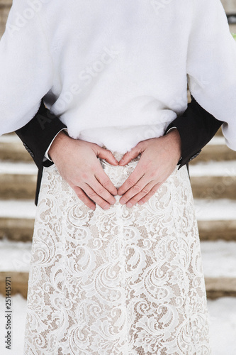 Closeup of romantic bride and groom hugging outside on winter day. Woman wearing white cozy faux fur coat.
