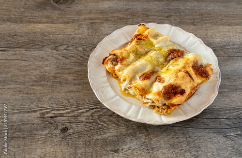 Cannelloni, Italian pasta pastry tubes stuffed with mince meat with white bechamel sauce and cheese crust, in the plate on the old wooden background.