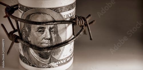 100 US Dollar bills wrapped with barbed wire as symbol of economic warfare, sanctions and embargo busting photo