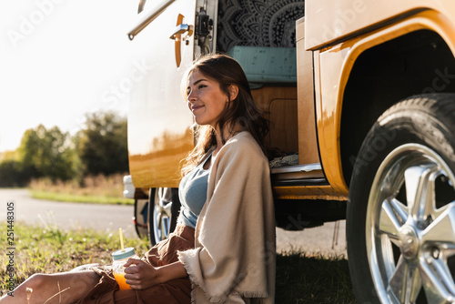 Pretty woman on a road trip with her camper, taking a break, drinking juice photo