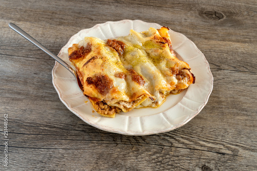 Cannelloni, Italian pasta pastry tubes stuffed with mince meat with white bechamel sauce and cheese crust, in the plate on the old wooden background.