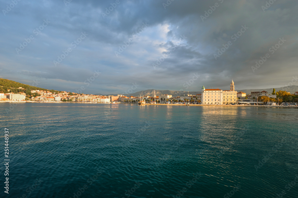 Fototapeta premium Sunrise view of the Riva Promenade, the Split Cathedral Tower and the old town section of Split, Croatia from the harbor on the Adriatic Sea