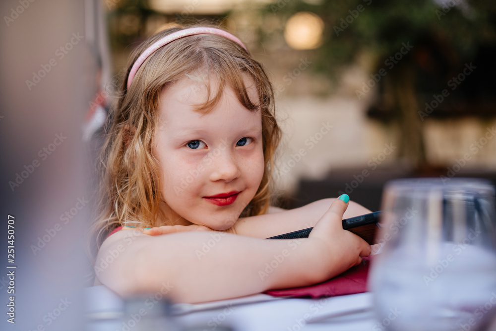 Portrait of cute girl with mobile phone sitting at sidewalk cafe in city