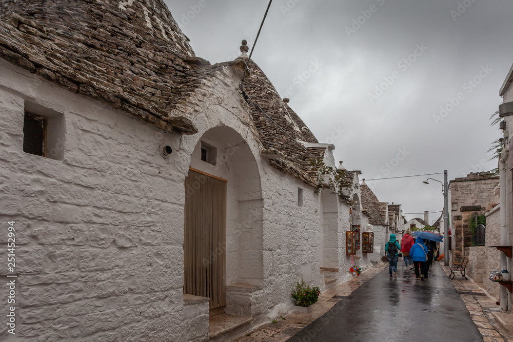 Tourists in the rain as they visit the streets of the Alberobello village, Puglia, Italy